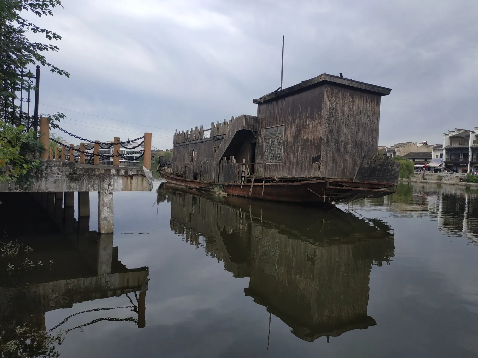 Old wooden buildings and a moored boat reflected in the water at Jinggang Ancient Town