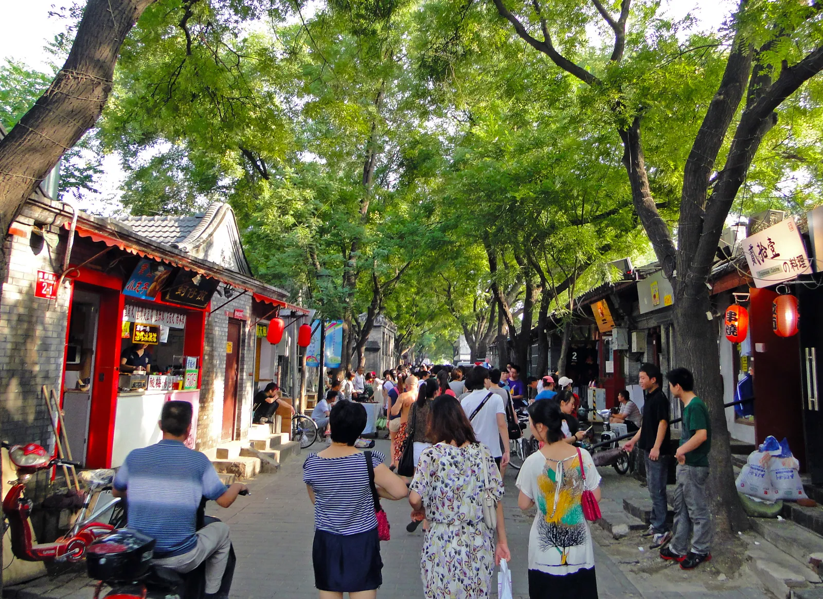 Tree-lined Nanluoguxiang lane with shops and strolling visitors