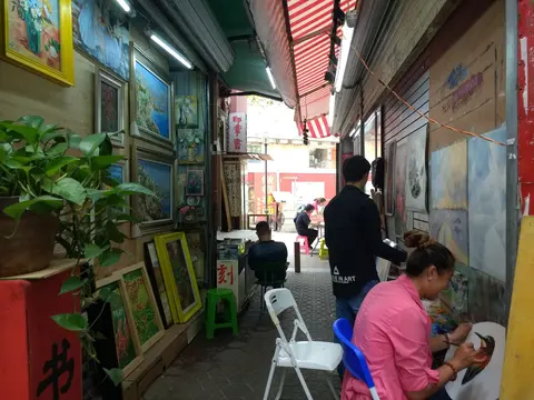 An alley in Dafen Oil Painting Village lined with canvases and working painters