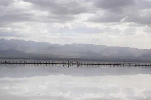 Mountains and clouds mirrored in the shallow water of Chaka Salt Lake