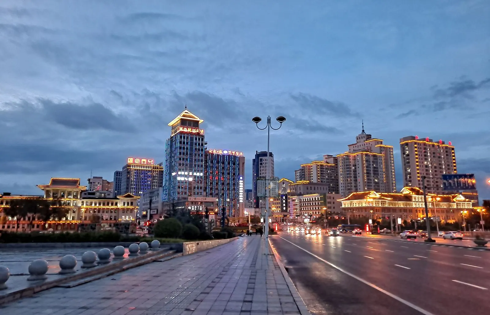 Downtown Yanji at dusk, with lit-up towers and Korean-style roofs along a wide avenue